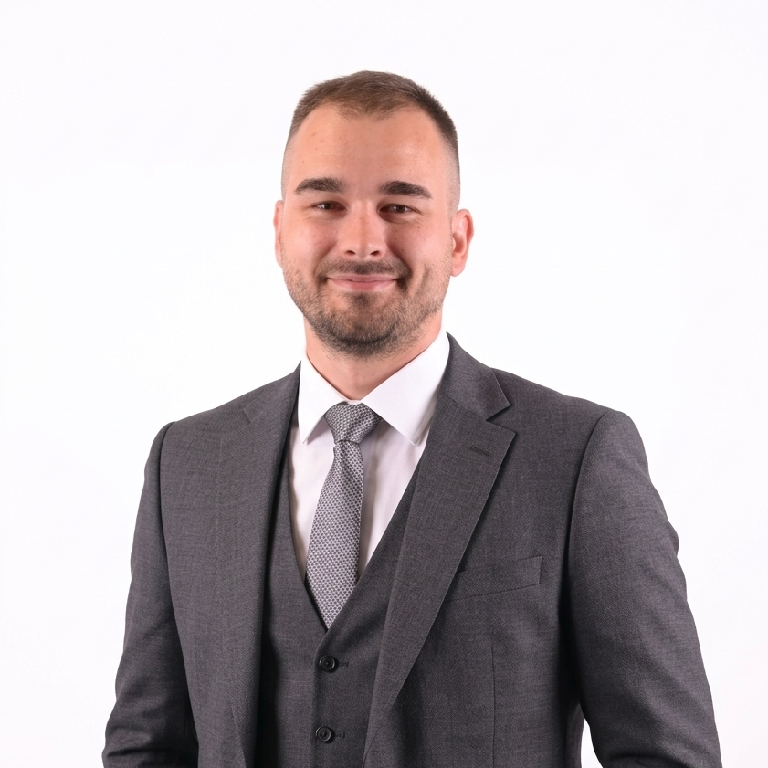 Smiling man in a gray suit and tie standing against a white background, presenting a professional portrait.